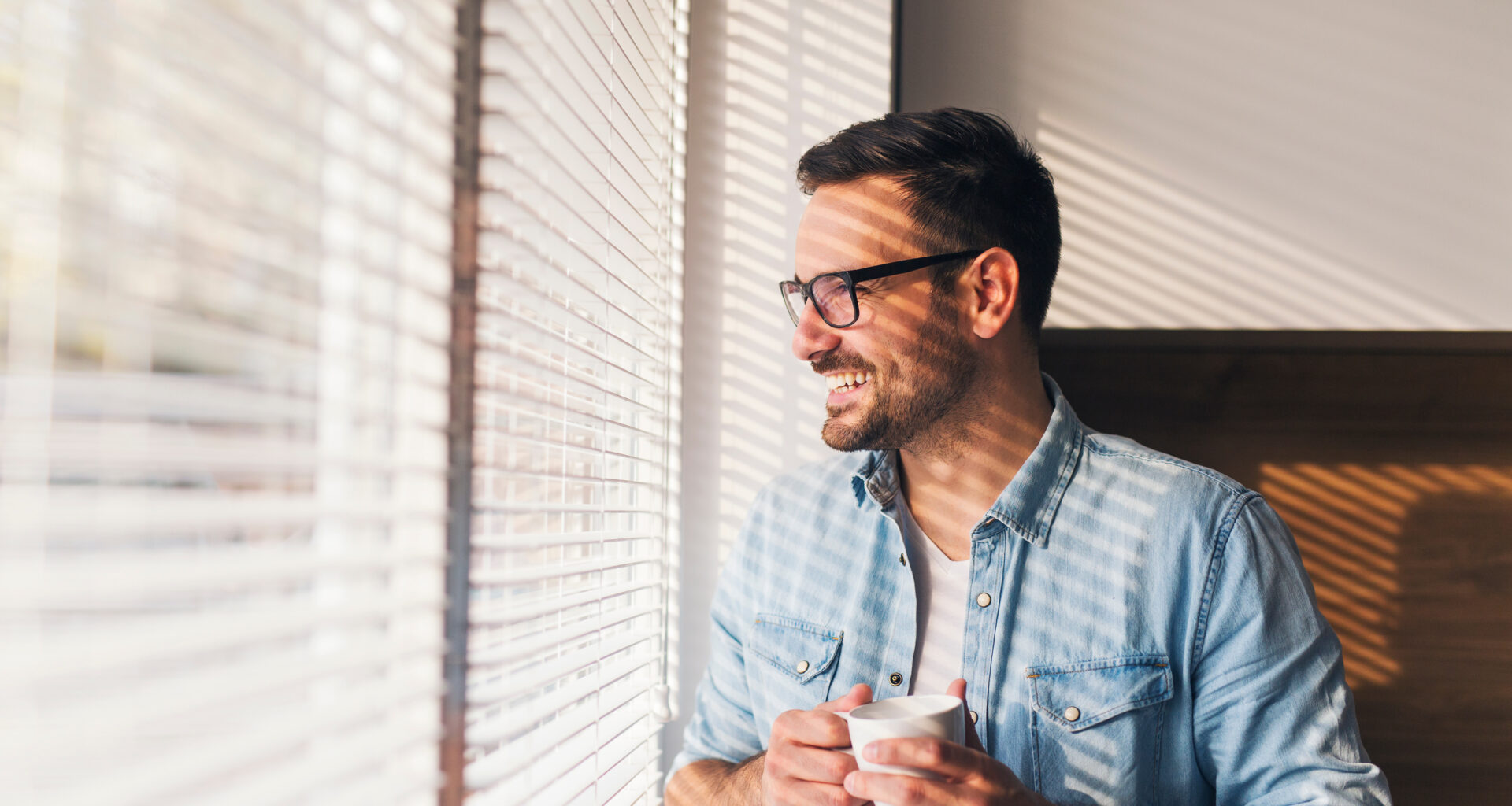 hombre mirando por la ventana con una taza de cafe en la mano