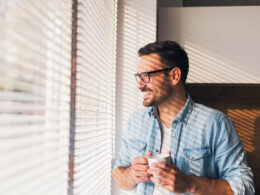 hombre mirando por la ventana con una taza de cafe en la mano