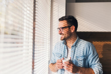 hombre mirando por la ventana con una taza de cafe en la mano