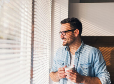 hombre mirando por la ventana con una taza de cafe en la mano