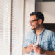 hombre mirando por la ventana con una taza de cafe en la mano